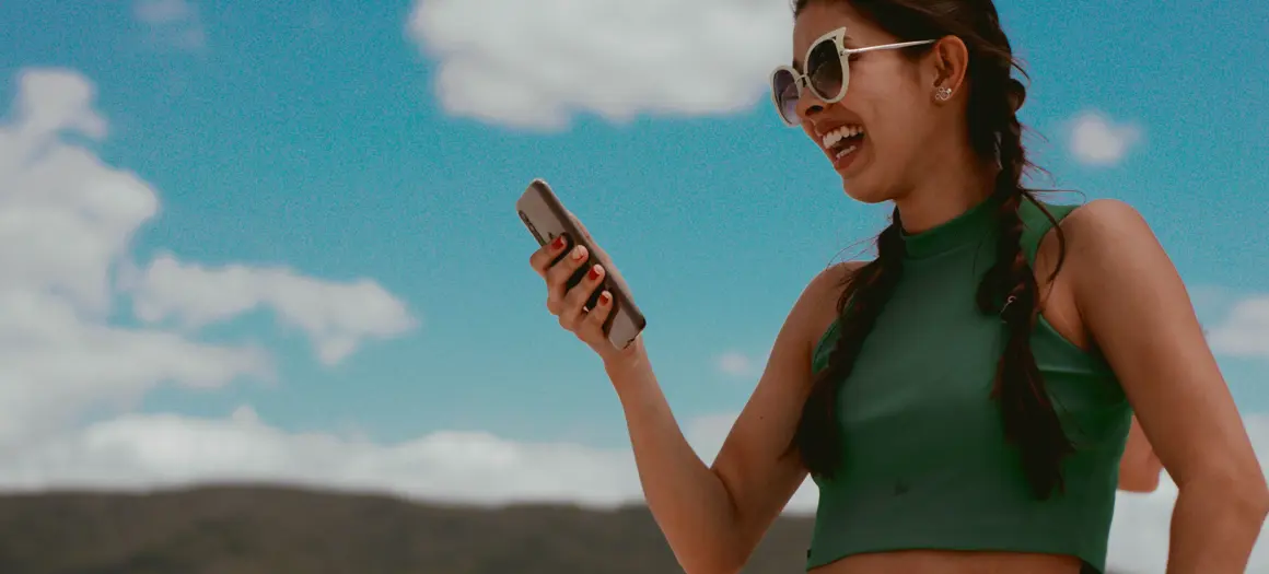 Vrouw lachend buiten met telefoon in hand