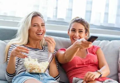 Twee vrouwen kijken lachen tv met popcorn en afstandsbediening