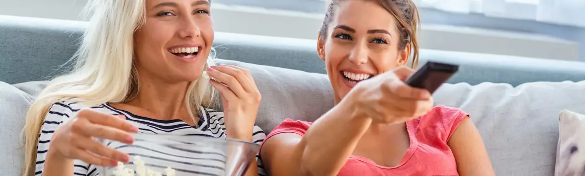 Twee vrouwen kijken lachen tv met popcorn en afstandsbediening
