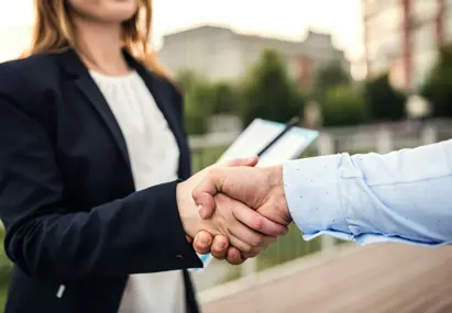 Ingezoomd beeld van vrouw met wit shirt en zwart colbert die een stevige hand geeft aan man in lichtblauw overhemd
