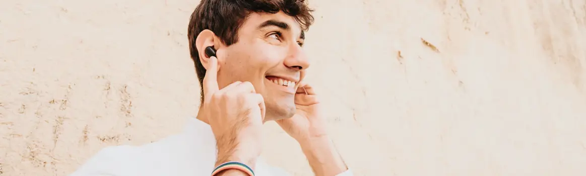 Man met witte trui heeft zijn handen tegen zijn oortjes en glimlacht