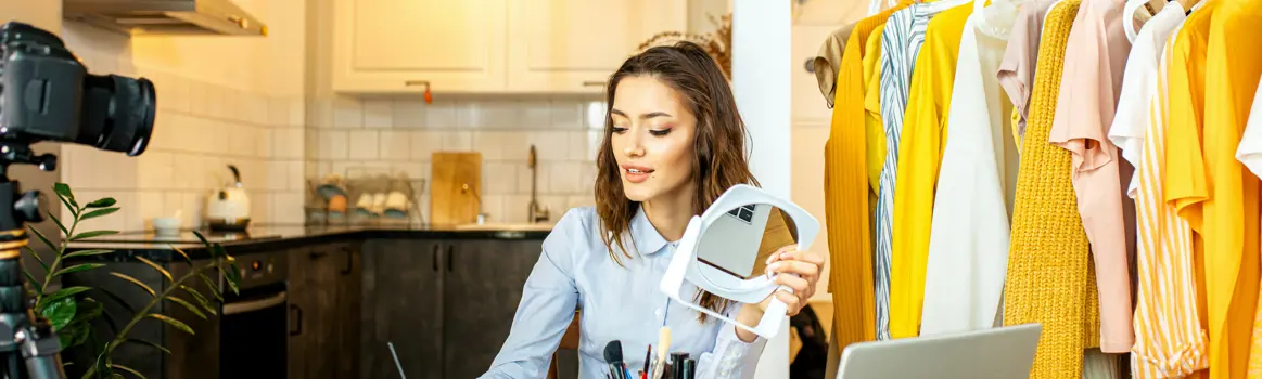 Vrouw maakt beautyvideo met make-up en statiefcamera, kledingrekken op de achtergrond