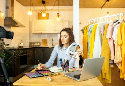 Vrouw maakt beautyvideo met make-up en statiefcamera, kledingrekken op de achtergrond