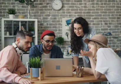 Vier personen aan een tafel kijkend naar een laptop