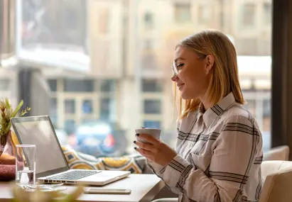 Vrouw aan tafel achter laptop met witte mok