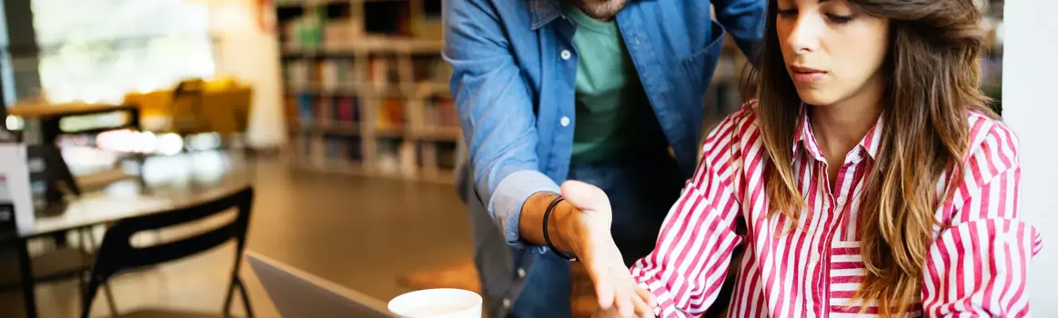man en vrouw achter een laptop die kijken naar een telefoonscherm